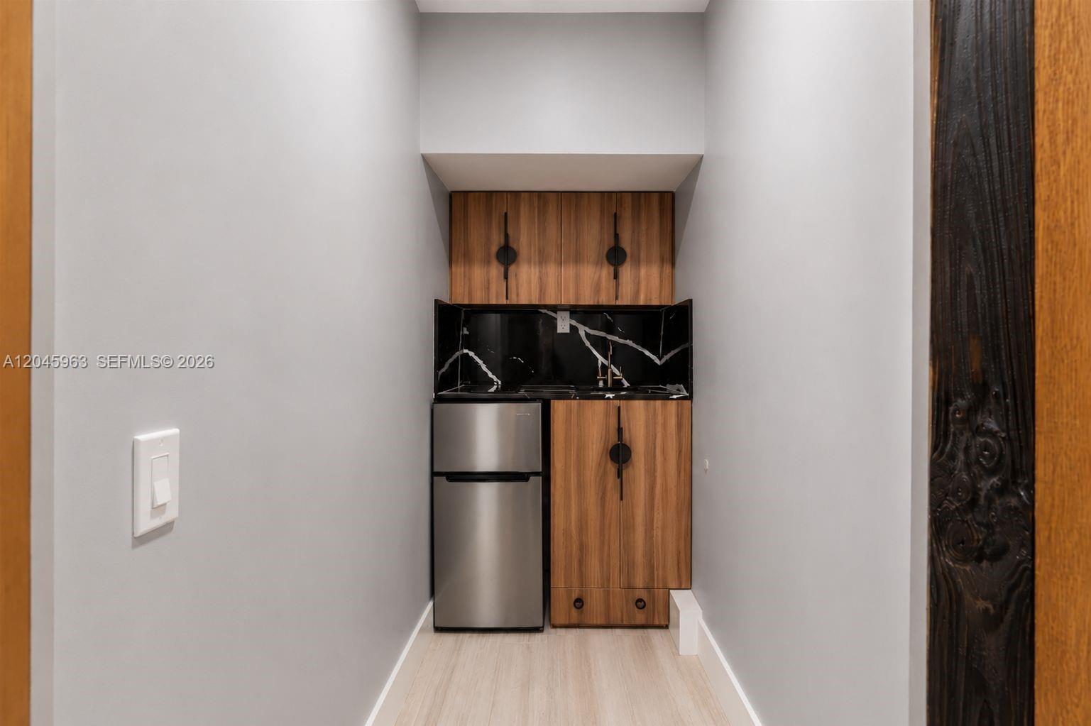 A small kitchenette features wood cabinets, a black marble backsplash, and a stainless steel refrigerator — 14888 SW 140th St # 1, Miami FL 33196, MIAMI, FL
