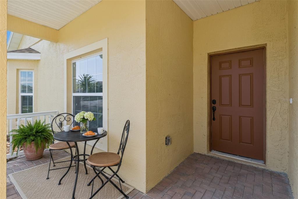 A small patio with a bistro set and potted plant sits beside a brown door — 4436 WATERFORD DRIVE, LAKE WALES, FL