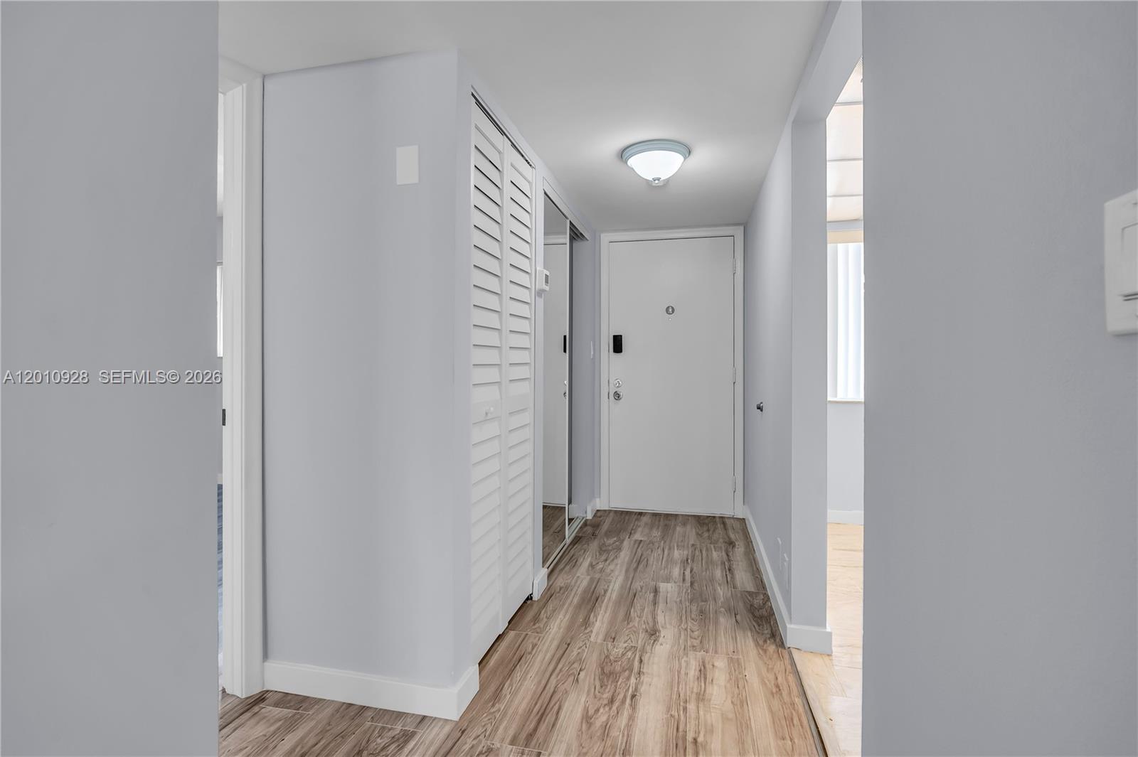 A hallway with light wood-look flooring, a white door, and louvered closet doors — 3571 Inverrary Dr # 202, Lauderhill FL 33319, LAUDERHILL, FL