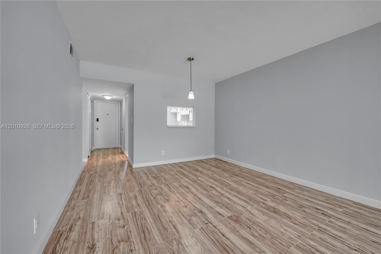 An empty room features light gray walls, wood-look tile flooring, and a small pass-through window — 3571 Inverrary Dr # 202, Lauderhill FL 33319, LAUDERHILL, FL