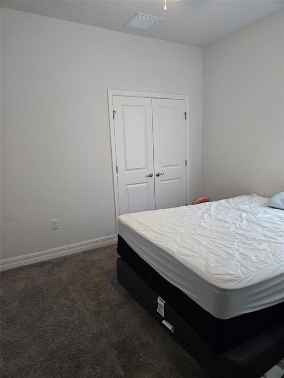 A bedroom features a bed with a white mattress, gray carpet, and white closet doors — 40 ORCHID LANE, POINCIANA, FL