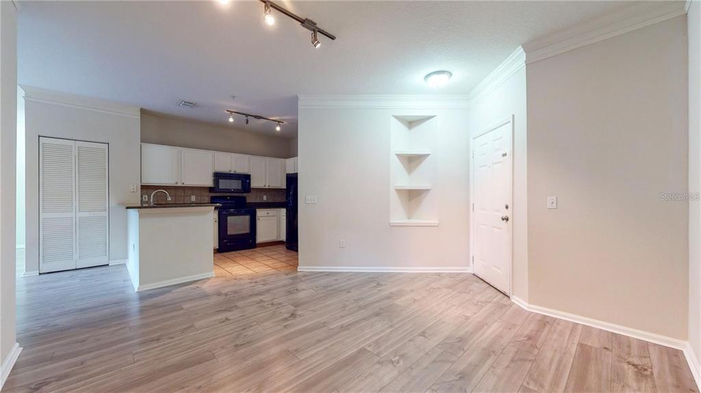 An open-concept living area features light wood-look flooring, a kitchen with dark appliances, and built-in shelving — 4207 S DALE MABRY HIGHWAY UNIT 3110, TAMPA, FL