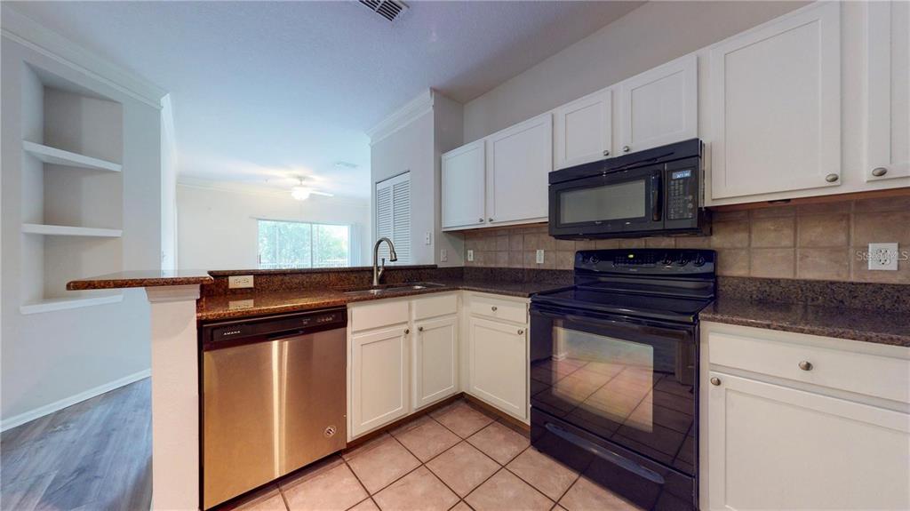A kitchen features white cabinets, granite countertops, stainless steel appliances, and a tiled floor — 4207 S DALE MABRY HIGHWAY UNIT 3110, TAMPA, FL