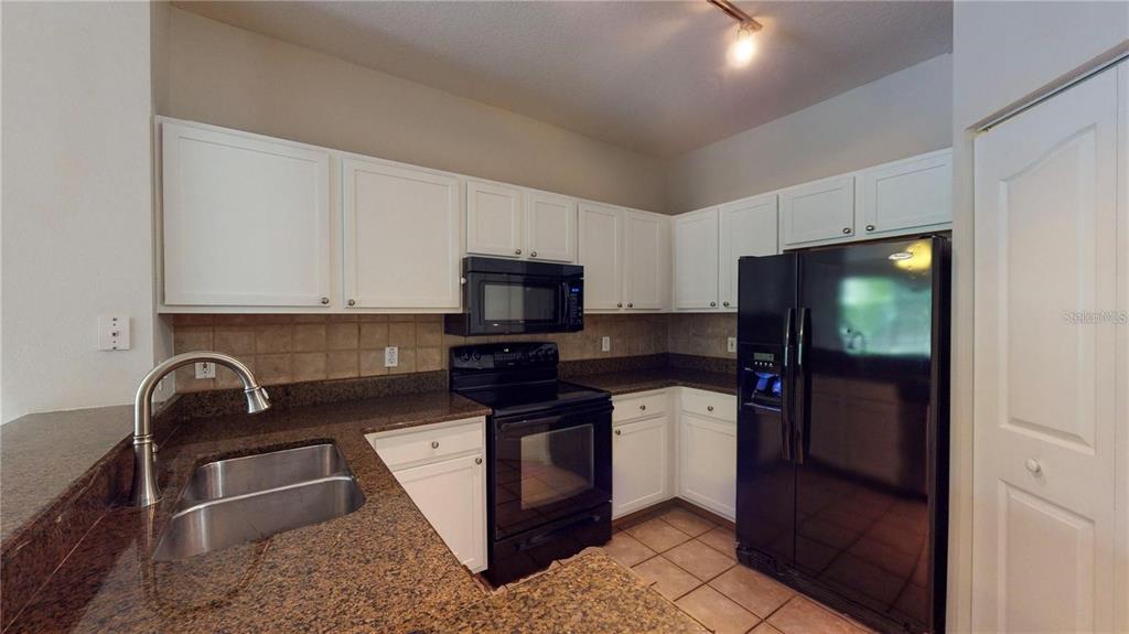 A kitchen features white cabinets, dark granite countertops, black appliances, and a double-basin sink — 4207 S DALE MABRY HIGHWAY UNIT 3110, TAMPA, FL