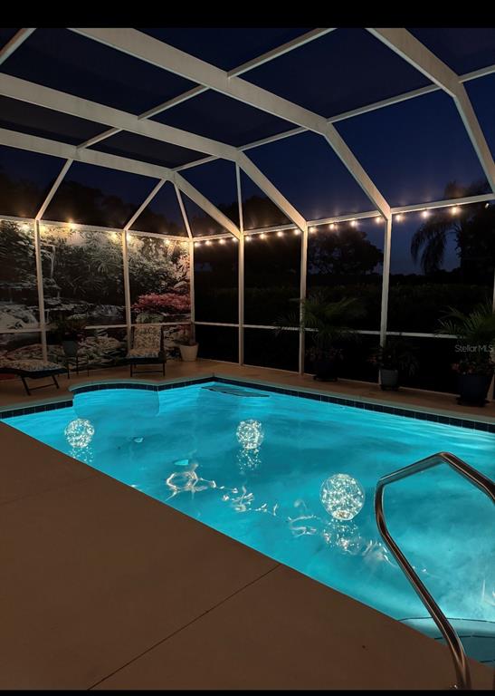 A swimming pool with floating lights is enclosed by a screened lanai at night — 13932 SE 96TH CIRCLE, SUMMERFIELD, FL