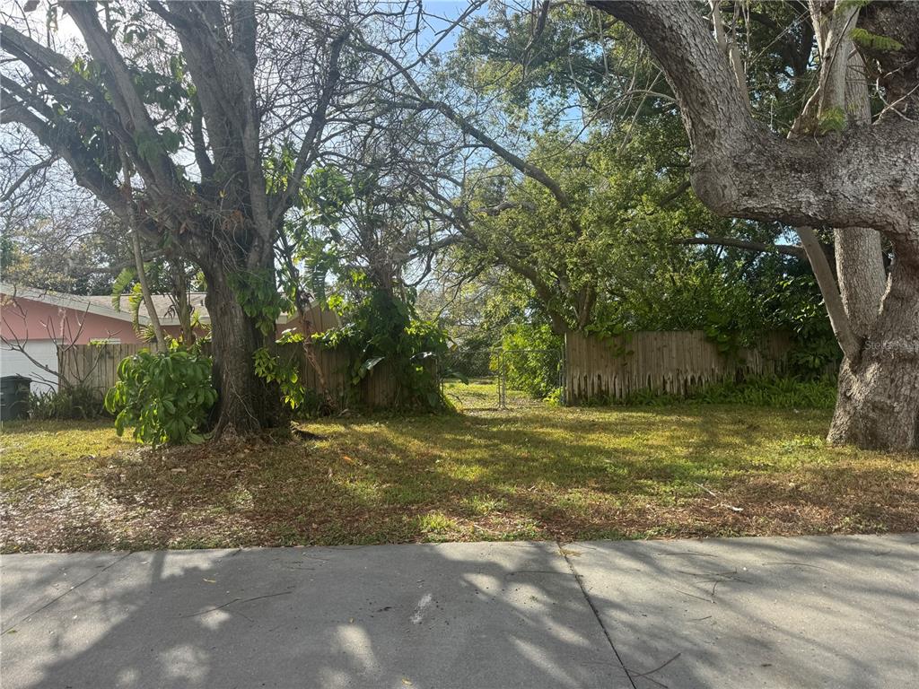 A vacant, grassy lot is framed by large trees and a wooden fence — 1546 BELLEAIR ROAD, CLEARWATER, FL
