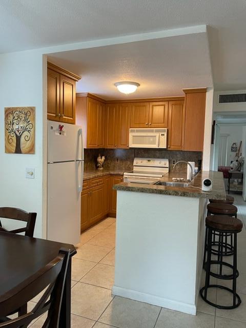 A kitchen features wood cabinets, white appliances, a breakfast bar, and tile flooring — 348 Monaco H, Delray Beach FL 33446, DELRAY BEACH, FL