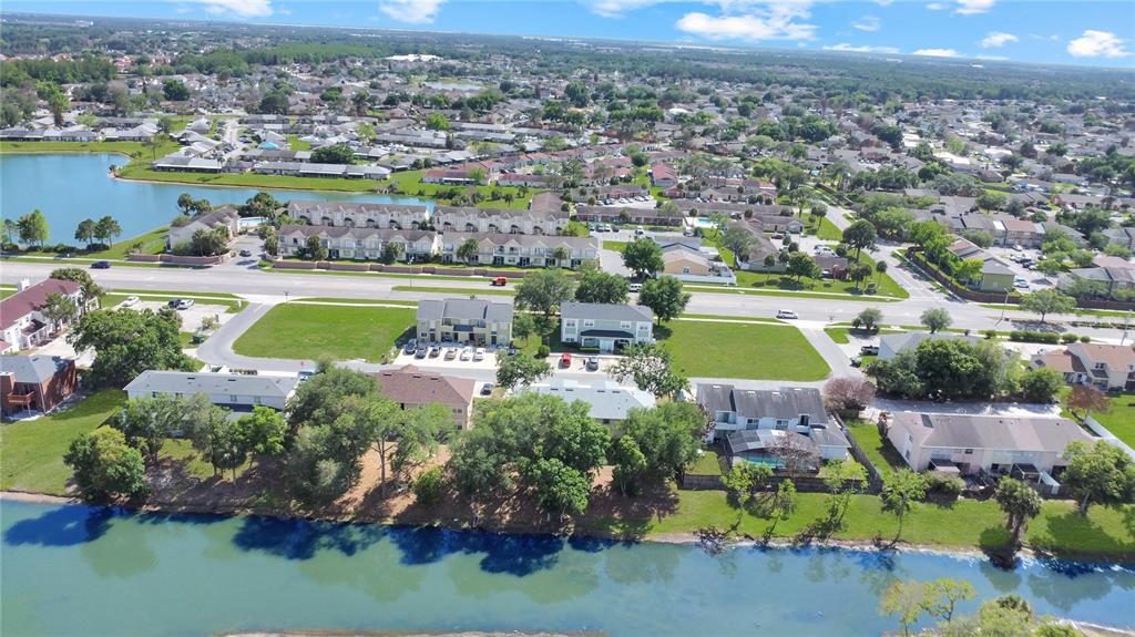 An aerial view shows residential buildings, green lawns, and a lake in a suburban neighborhood — 206 MAJORS LANE UNIT D, KISSIMMEE, FL