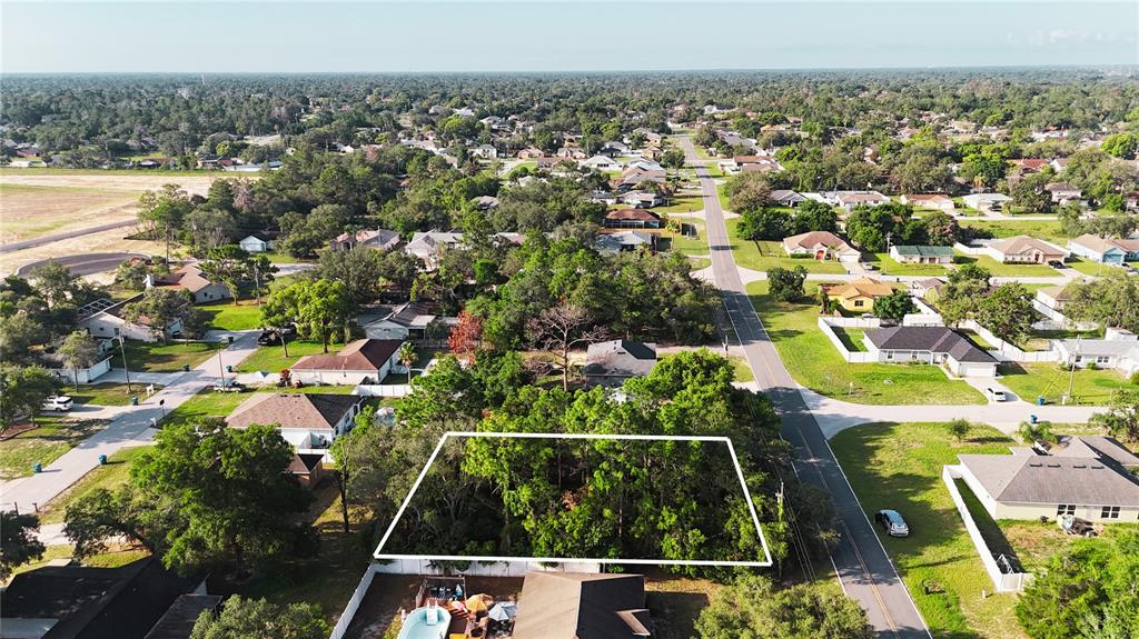 An aerial view shows a wooded, rectangular vacant lot outlined in white within a residential neighborhood — 3581 LEMA DRIVE, SPRING HILL, FL