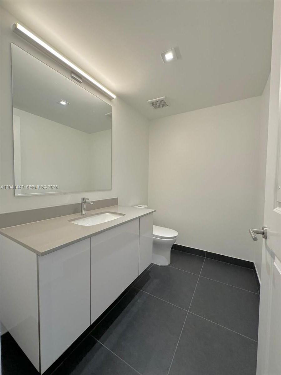 A modern bathroom features a white vanity, a large mirror, and dark floor tiles — 1600 NE 1st Ave # 3205, Miami FL 33132, MIAMI, FL