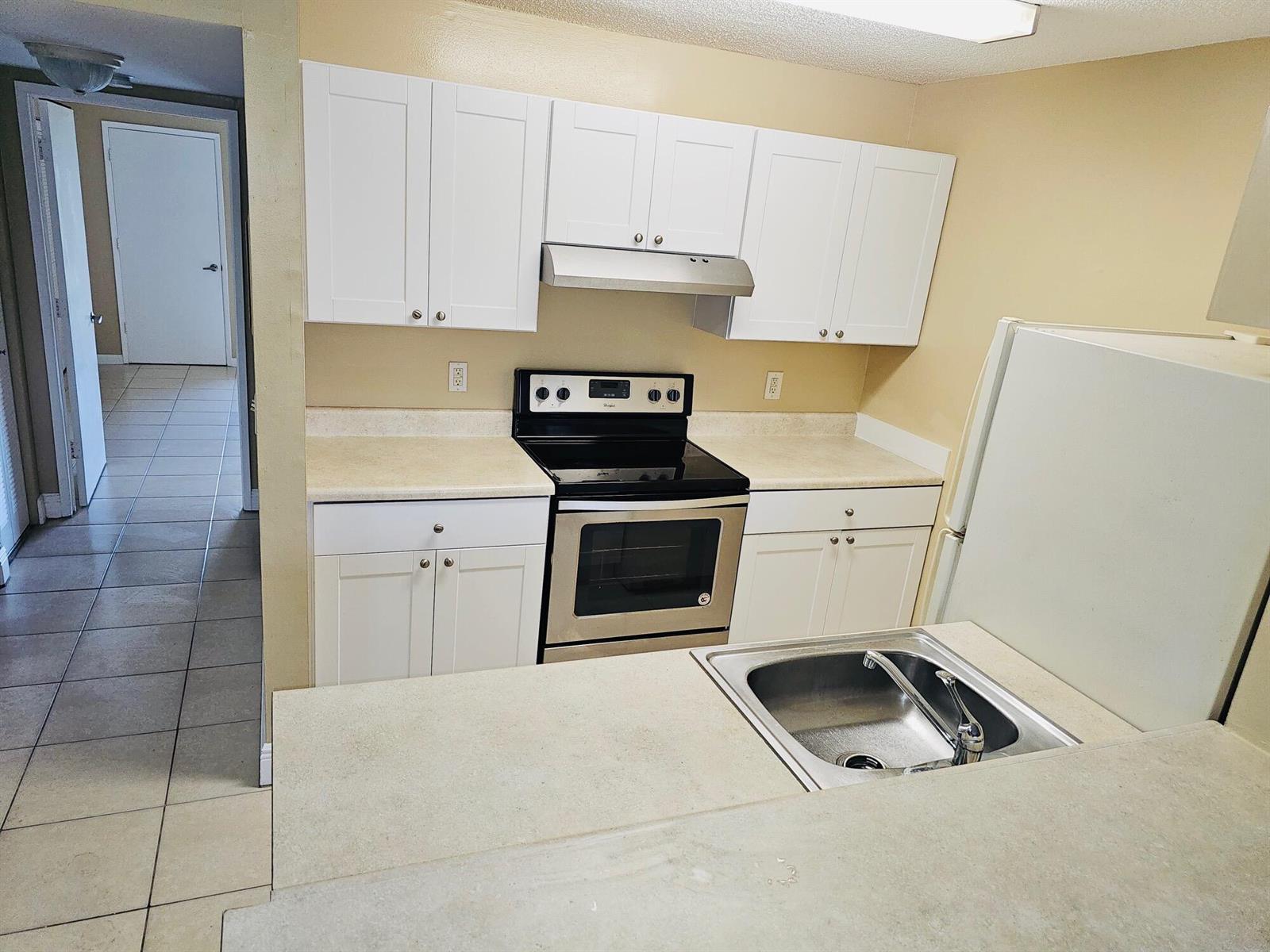 A kitchen features white cabinets, stainless steel appliances, and beige countertops — 1605 Meadows Circle W # 1605, Boynton Beach FL 33436, BOYNTON BEACH, FL