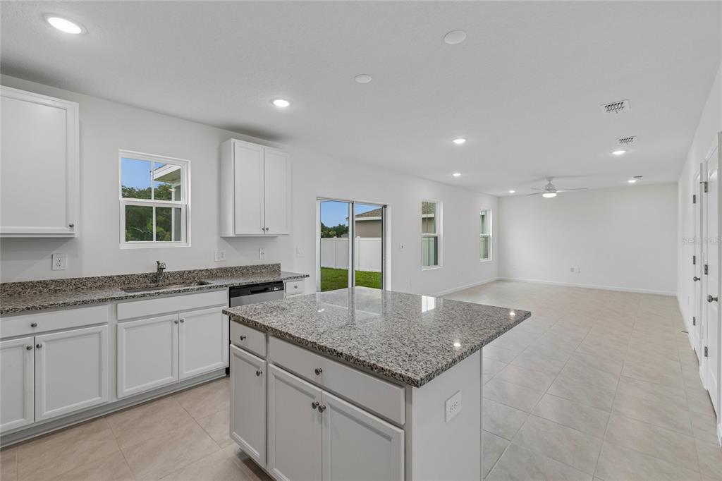 A kitchen with white cabinets, granite countertops, and an island opens to a living area — 3139 REIN AVENUE, DAVENPORT, FL