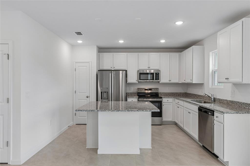 A kitchen with white cabinets, granite countertops, stainless steel appliances, and a central island — 3139 REIN AVENUE, DAVENPORT, FL