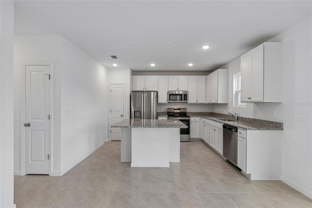 A modern kitchen features white cabinets, granite countertops, stainless steel appliances, and a central island — 3139 REIN AVENUE, DAVENPORT, FL