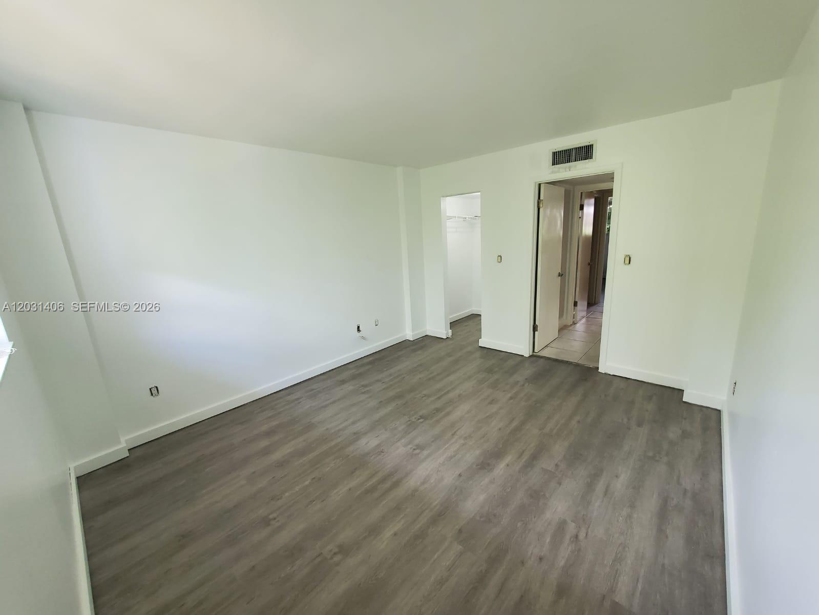 An empty room features white walls, gray wood-look flooring, a walk-in closet, and a doorway — 750 NE 64th St # B511, Miami FL 33138, MIAMI, FL