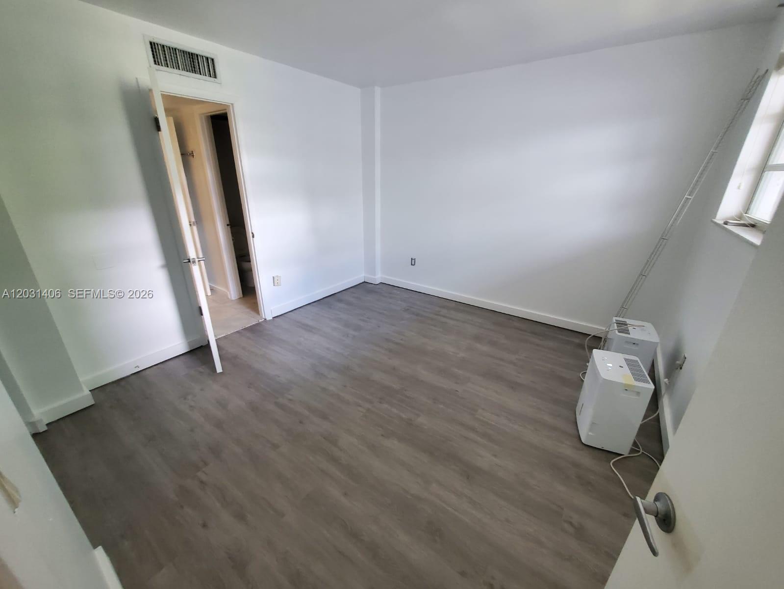An empty room with white walls, gray wood-look flooring, and two portable air conditioning units — 750 NE 64th St # B511, Miami FL 33138, MIAMI, FL