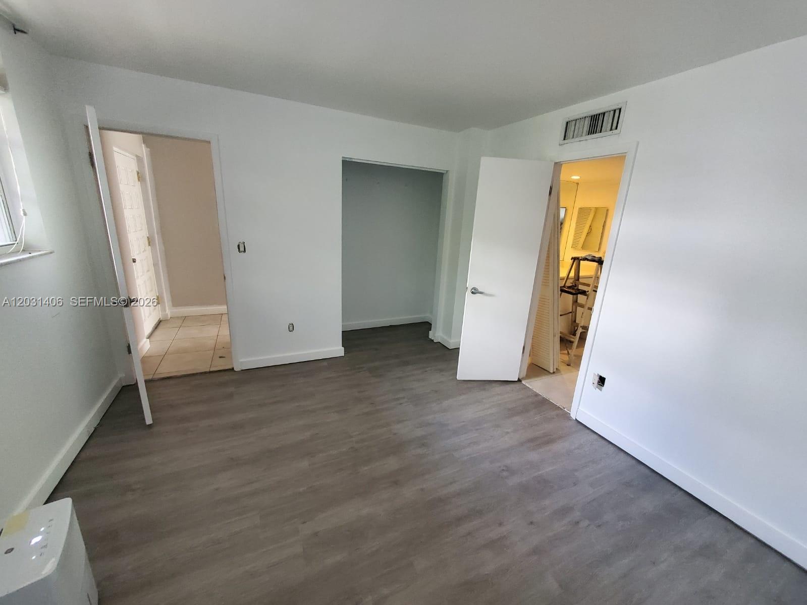 A bedroom with gray wood-look flooring, white walls, a closet, and two doorways — 750 NE 64th St # B511, Miami FL 33138, MIAMI, FL