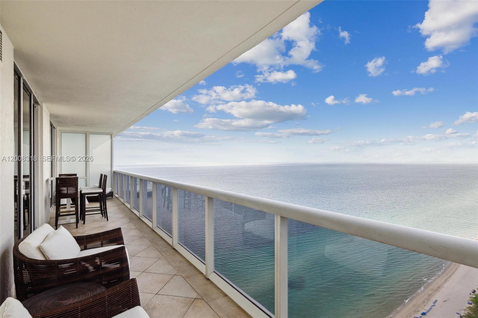 A balcony with wicker furniture overlooks the ocean under a blue sky with clouds — 1830 S OCEAN DR # 4803, Hallandale Beach FL 33009, HALLANDALE BEACH, FL