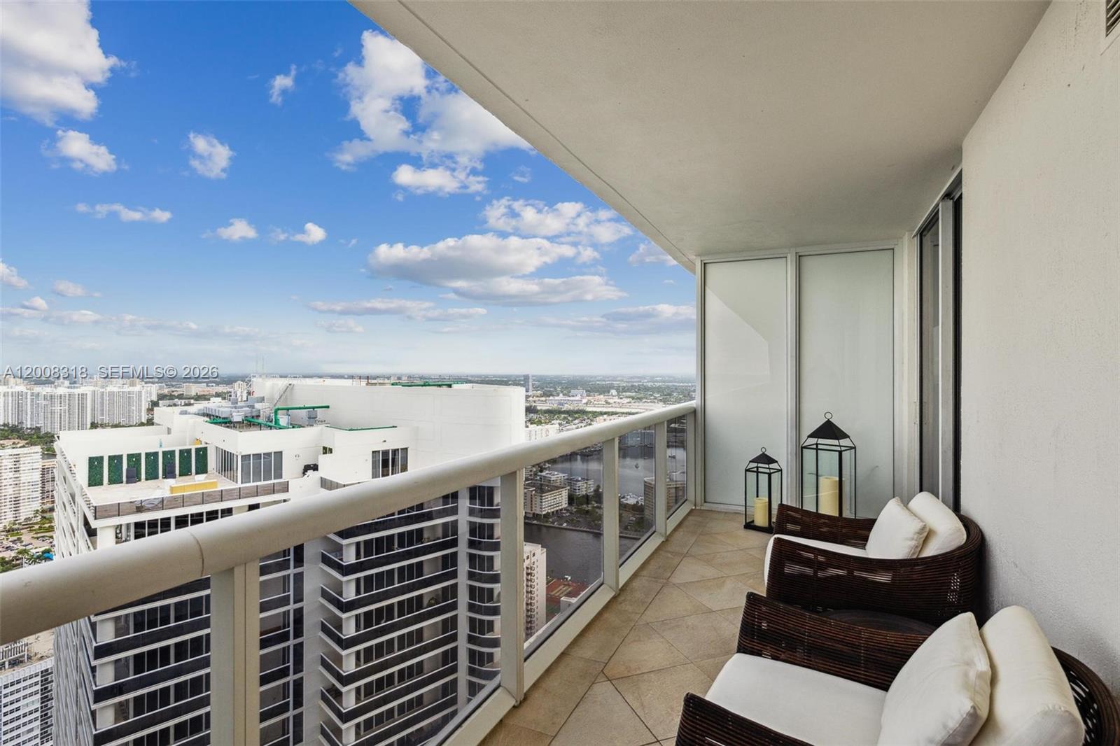 A high-rise balcony features two wicker chairs, lanterns, and a view of city buildings — 1830 S OCEAN DR # 4803, Hallandale Beach FL 33009, HALLANDALE BEACH, FL