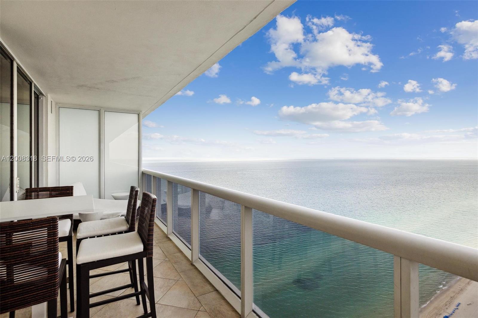A balcony with outdoor furniture overlooks the ocean under a blue sky with clouds — 1830 S OCEAN DR # 4803, Hallandale Beach FL 33009, HALLANDALE BEACH, FL