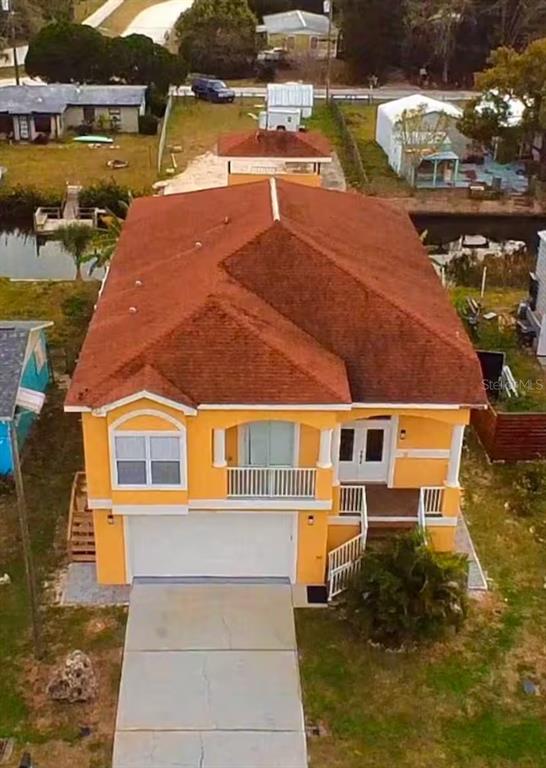 An elevated, orange-colored house with a red roof, a white garage door, and a driveway — 7322 SHEEPSHEAD DRIVE, HUDSON, FL