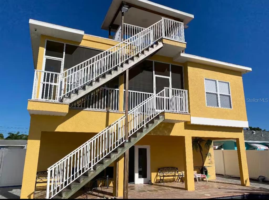 A three-story yellow house features exterior staircases leading to screened balconies and a rooftop deck — 7322 SHEEPSHEAD DRIVE, HUDSON, FL