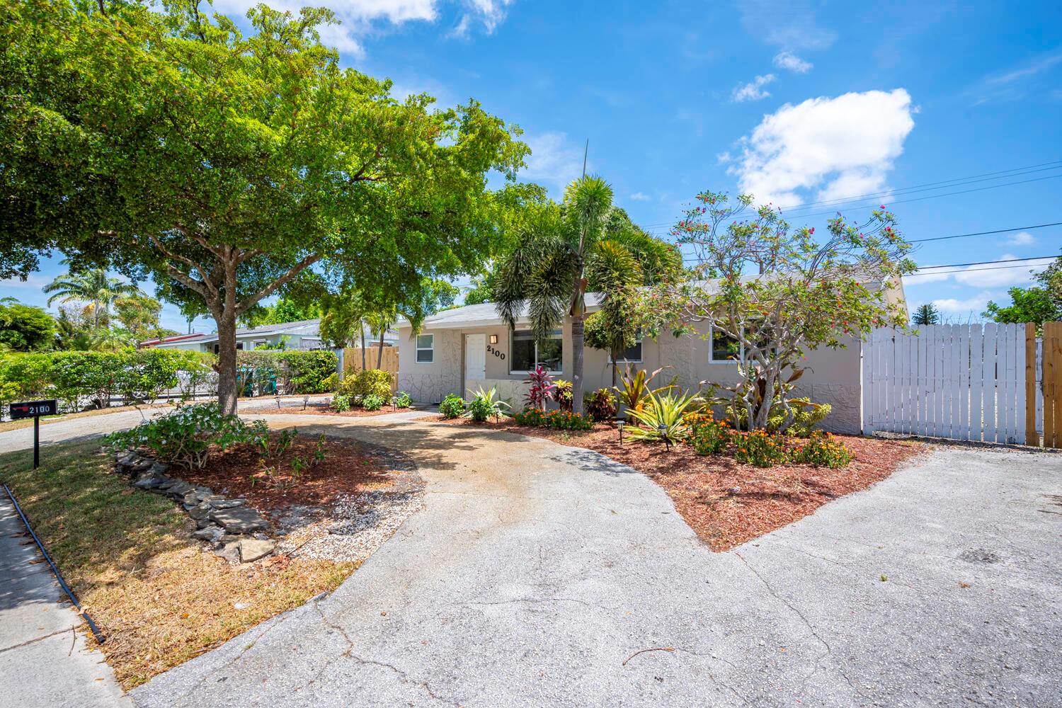 A single-story house with a concrete driveway, landscaping, and a white fence under a blue sky — 2100 N Seacrest Boulevard, Boynton Beach FL 33435, BOYNTON BEACH, FL