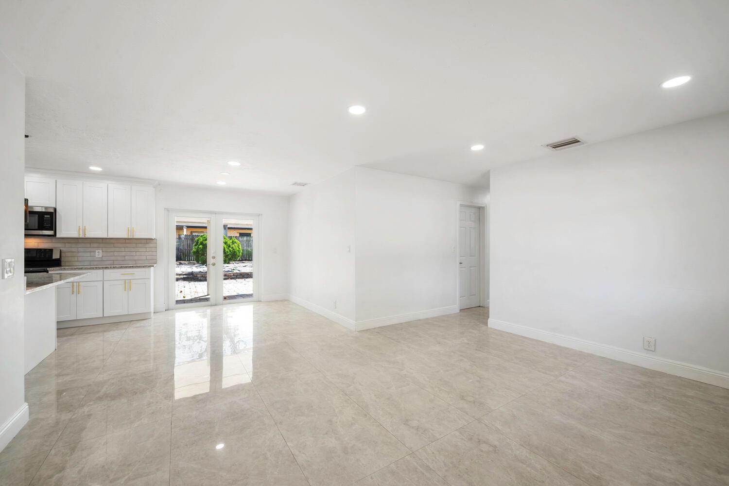 A bright, open-concept kitchen and living area featuring white cabinets, tile flooring, and glass doors — 2100 N Seacrest Boulevard, Boynton Beach FL 33435, BOYNTON BEACH, FL