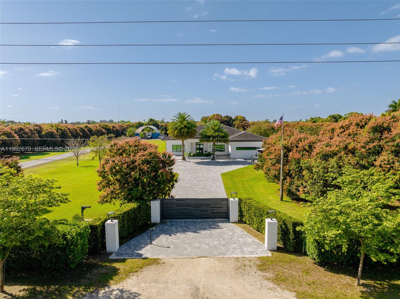 An aerial view shows a modern white house behind a gated driveway and lush trees — 17950 SW 192nd St, Miami FL 33187, MIAMI, FL