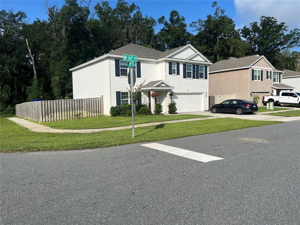 A two-story white house with blue shutters and a wooden fence on a corner lot — 19007 NW 164TH ROAD, HIGH SPRINGS, FL