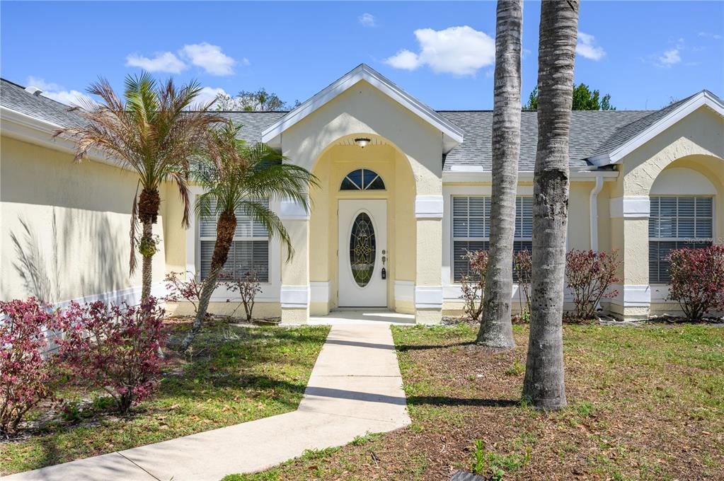 A single-story house with a white front door, arched entryway, and palm trees in front — 1831 OAKGROVE AVENUE, DELTONA, FL