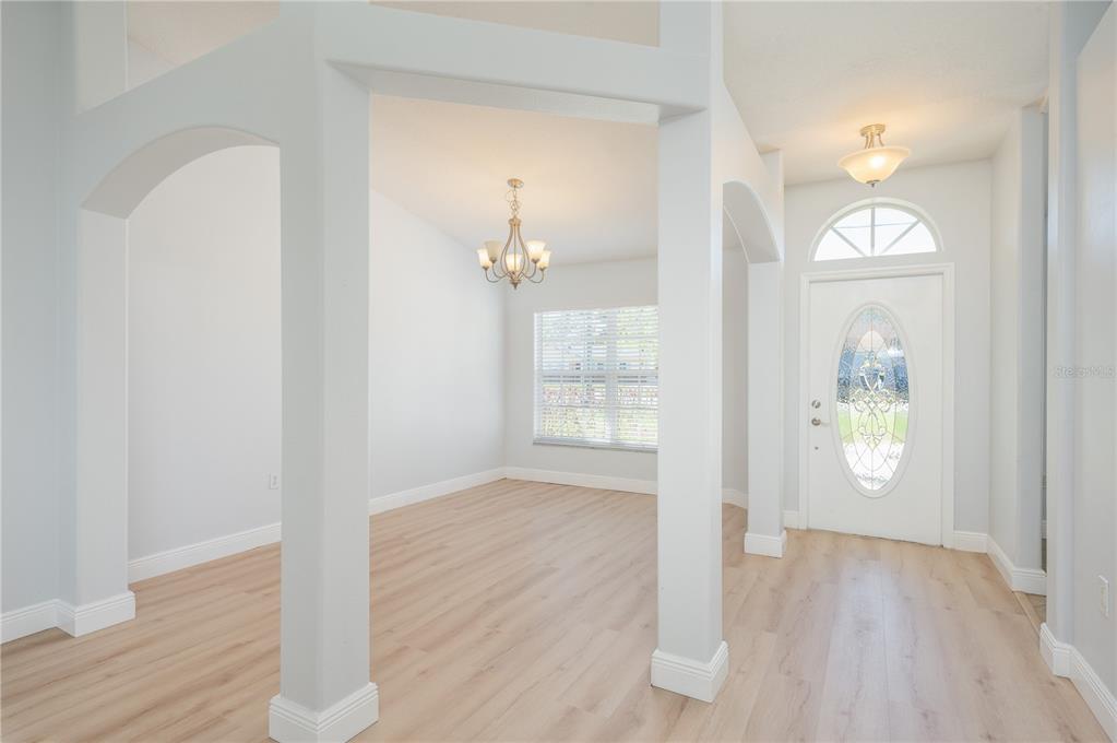 An entryway leads to a dining area with light wood flooring and a chandelier — 1831 OAKGROVE AVENUE, DELTONA, FL