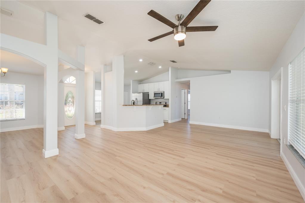 A spacious living room with light wood-look flooring, white walls, and an open kitchen — 1831 OAKGROVE AVENUE, DELTONA, FL
