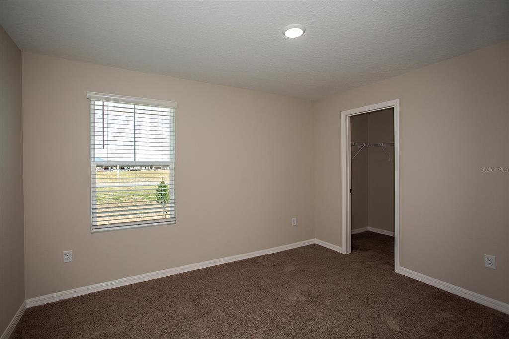 An empty bedroom features beige walls, brown carpeting, a window with blinds, and a closet — 4273 RIVER BEACON BOULEVARD, DAVENPORT, FL