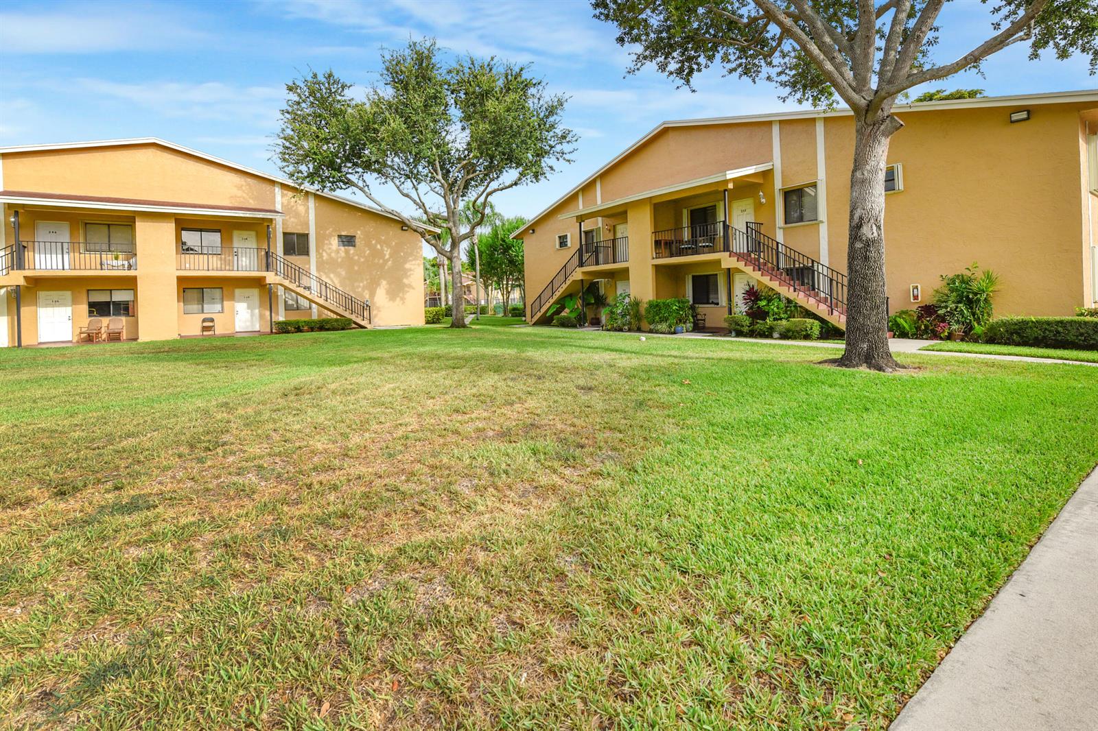 Two tan apartment buildings with exterior staircases face a grassy courtyard under a blue sky — 6053 10th 140 Avenue N # 140, FL 33463, FL