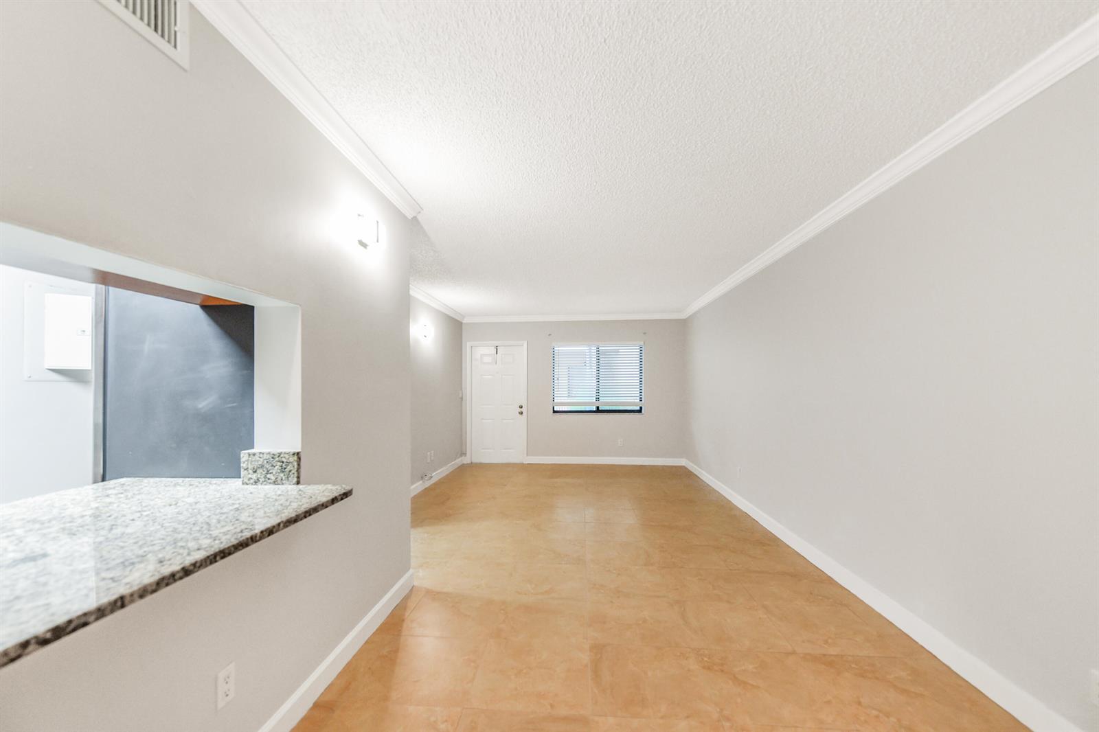 An empty living room features light-colored tile flooring, gray walls, and a granite breakfast bar — 6053 10th 140 Avenue N # 140, FL 33463, FL