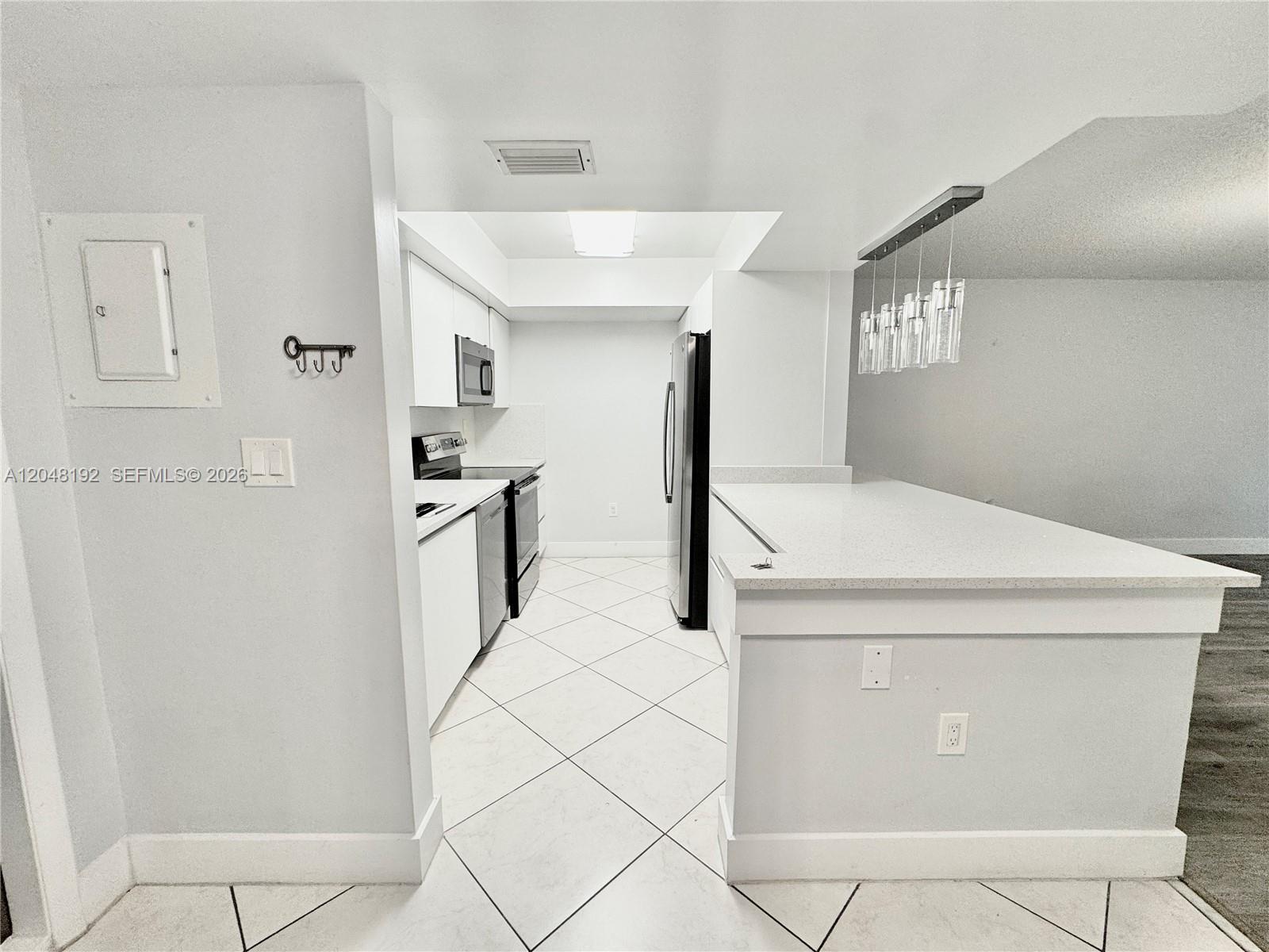 A white galley kitchen features stainless steel appliances, quartz countertops, and a breakfast bar — 8600 NW 34th Pl # B102, Sunrise FL 33351, SUNRISE, FL