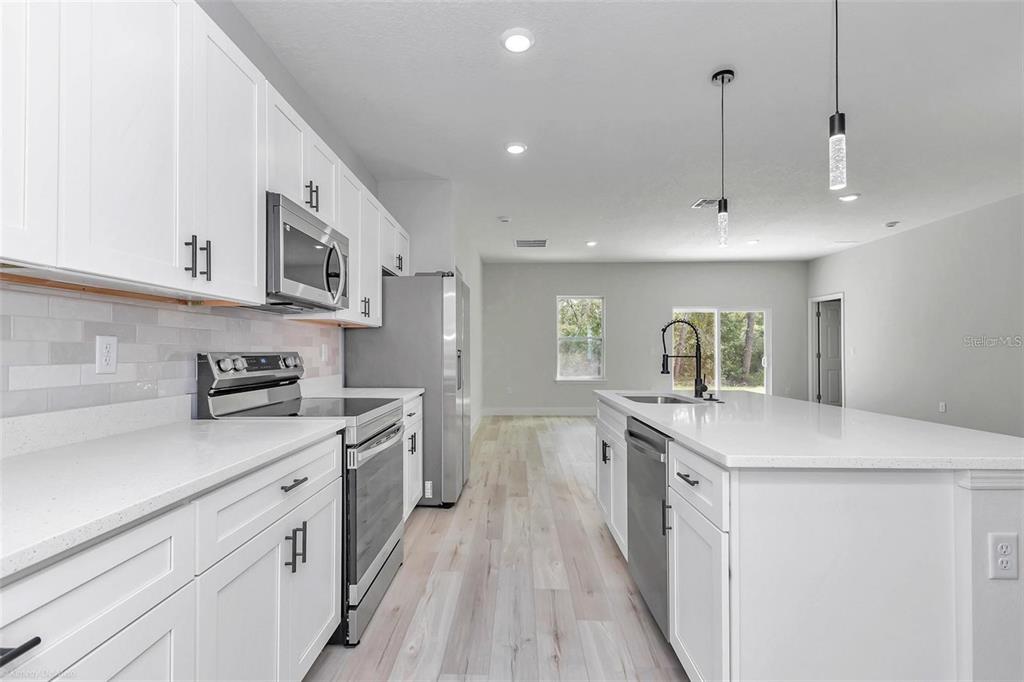 A modern kitchen features white cabinetry, stainless steel appliances, quartz countertops, and light wood flooring — 3398 SW 165TH LOOP, OCALA, FL