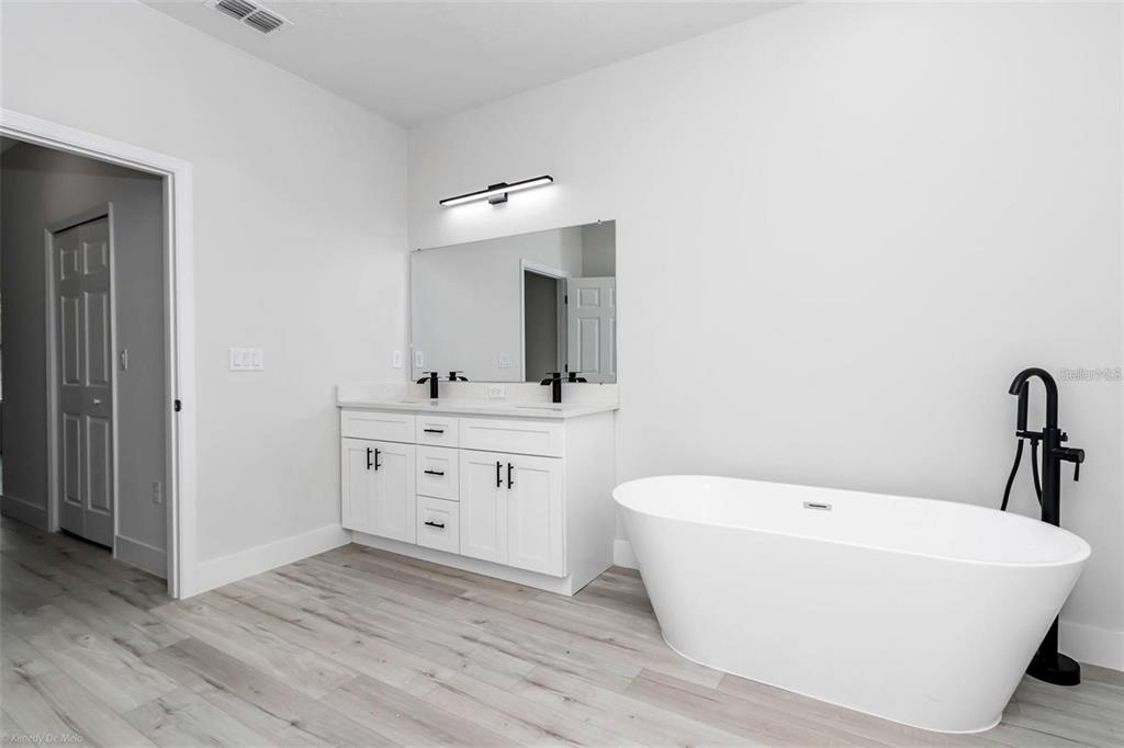 A modern bathroom features a white double vanity, a freestanding tub, and light wood flooring — 3398 SW 165TH LOOP, OCALA, FL