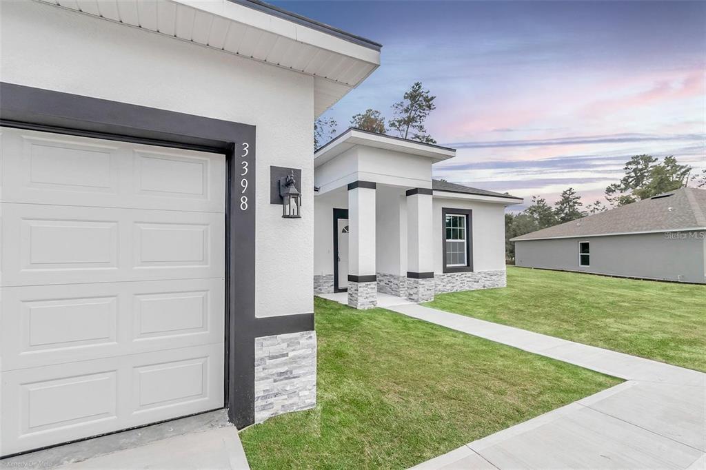 A modern single-story house exterior features white stucco walls, stone accents, and a garage — 3398 SW 165TH LOOP, OCALA, FL