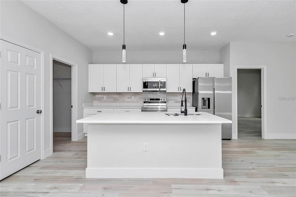A modern kitchen features white cabinetry, stainless steel appliances, a center island, and light flooring — 3398 SW 165TH LOOP, OCALA, FL
