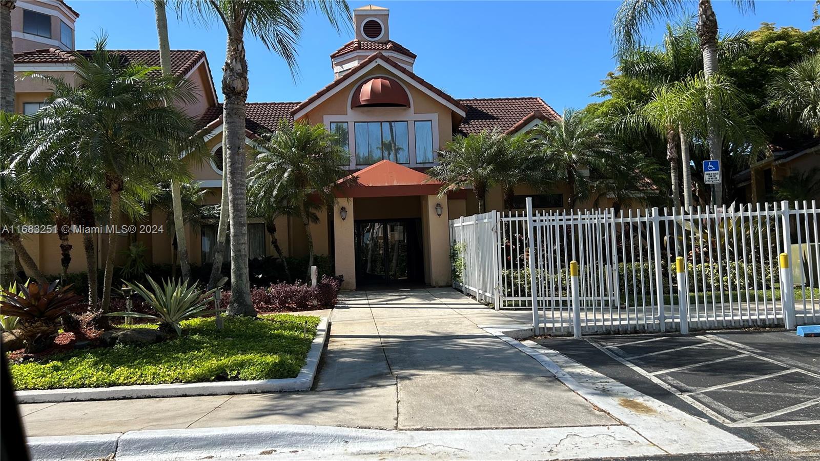 A tan building with a tiled roof and a white fence stands behind a sidewalk — 15551 SW 104th Ter # 828, Miami FL 33196, MIAMI, FL