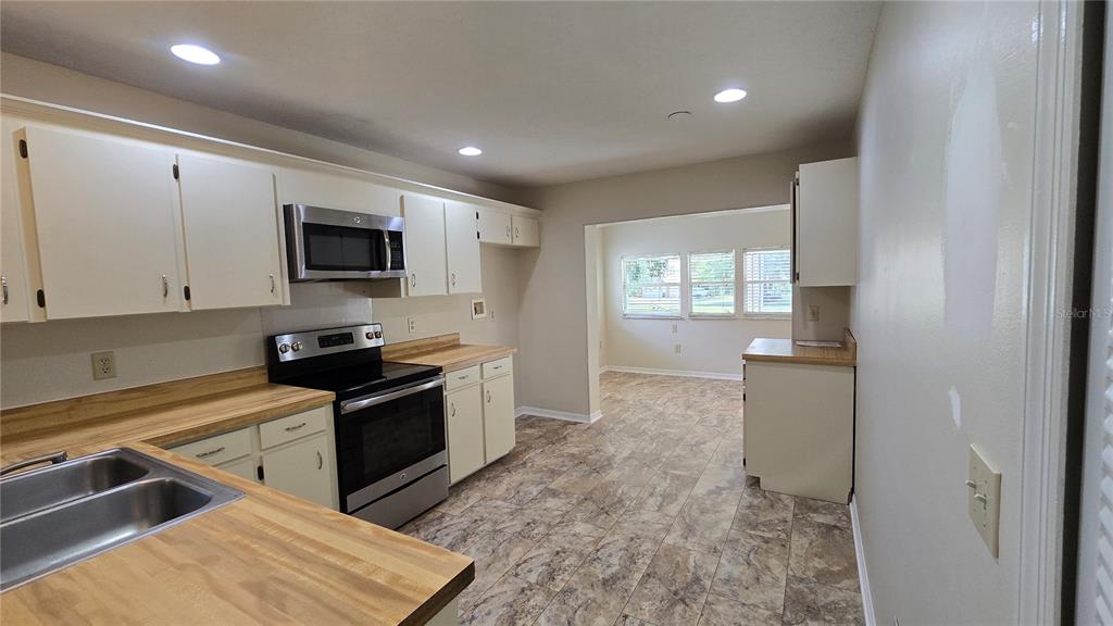 A kitchen features light-colored cabinets, wood-look laminate countertops, stainless steel appliances, and tile flooring — 1657 TREMONT LANE, WINTER PARK, FL