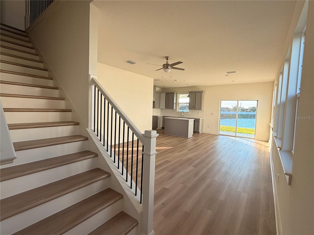 An open-concept living area features a staircase, wood-look flooring, and a kitchen overlooking a lake — 13763 EMERALD FIELDS DRIVE Lot 134, HUDSON, FL
