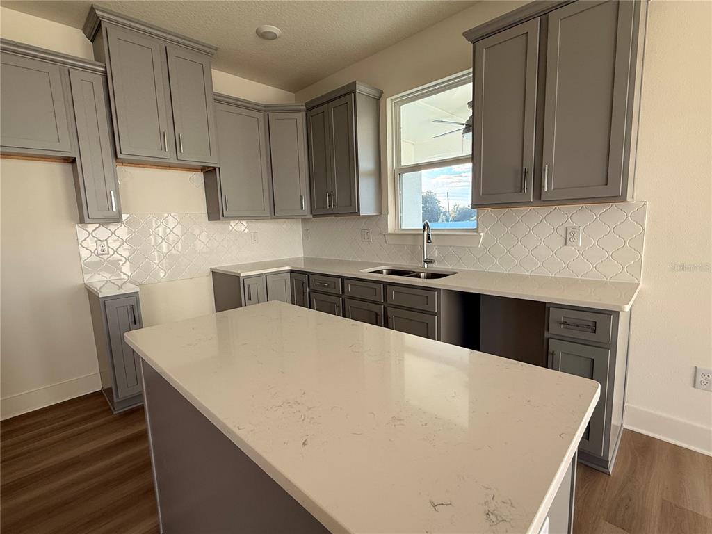 A kitchen features gray cabinets, white quartz countertops, and a white patterned tile backsplash — 13763 EMERALD FIELDS DRIVE Lot 134, HUDSON, FL