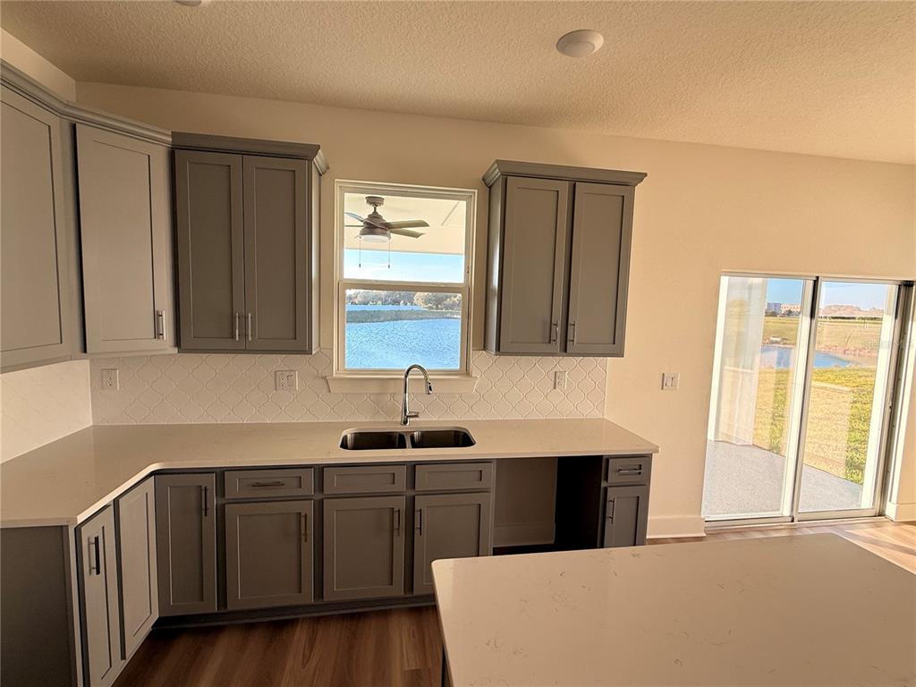 A kitchen features gray cabinets, white countertops, a tile backsplash, and a view of water — 13763 EMERALD FIELDS DRIVE Lot 134, HUDSON, FL