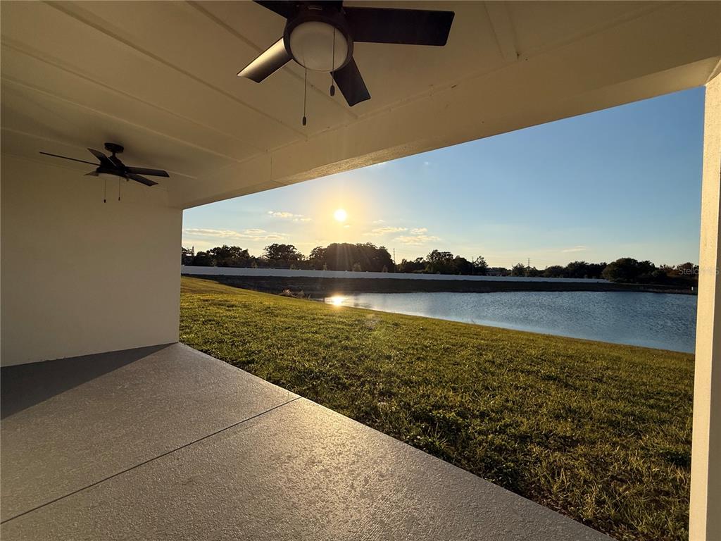 A covered patio overlooks a grassy lawn, a pond, and the setting sun — 13763 EMERALD FIELDS DRIVE Lot 134, HUDSON, FL