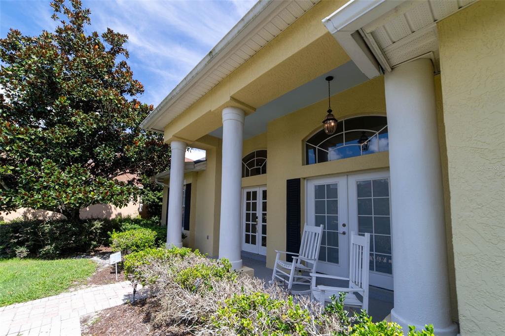 A covered front porch features white columns, two rocking chairs, and glass-paned double doors — 2960 ASHTON TERRACE, OVIEDO, FL