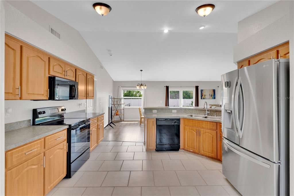 A kitchen with light wood cabinets, black appliances, and tile flooring opens to a dining area — 6315 HAMPTON POINTE CIRCLE, LAKELAND, FL