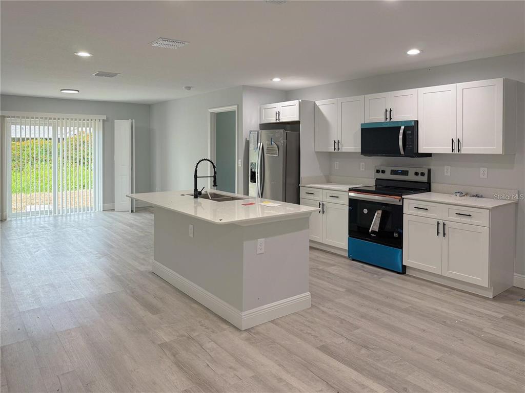 A modern kitchen features white cabinets, a central island, and light wood-look flooring — 608 COUGAR BOULEVARD, SEBRING, FL
